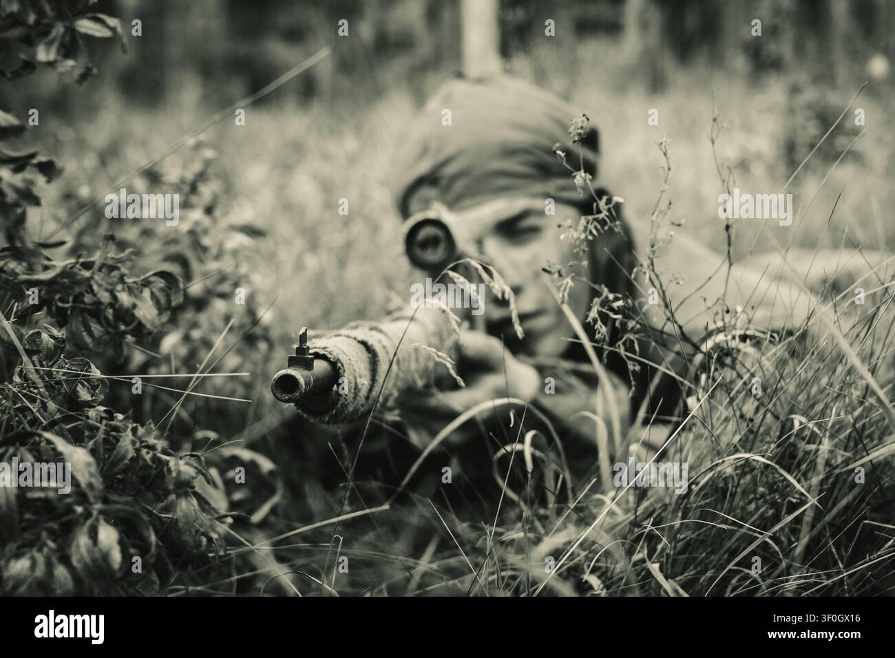 Sepiafarbene Aufnahme eines sowjetischen Scharfschützen, der ein Gewehr mit Zielfernrohr von einer grasbewachsenen Falle aus zielt. Geschichte des Zweiten Weltkriegs, Vintage-Kriegskino und Schlachtfeld-Spannung. Stockfoto