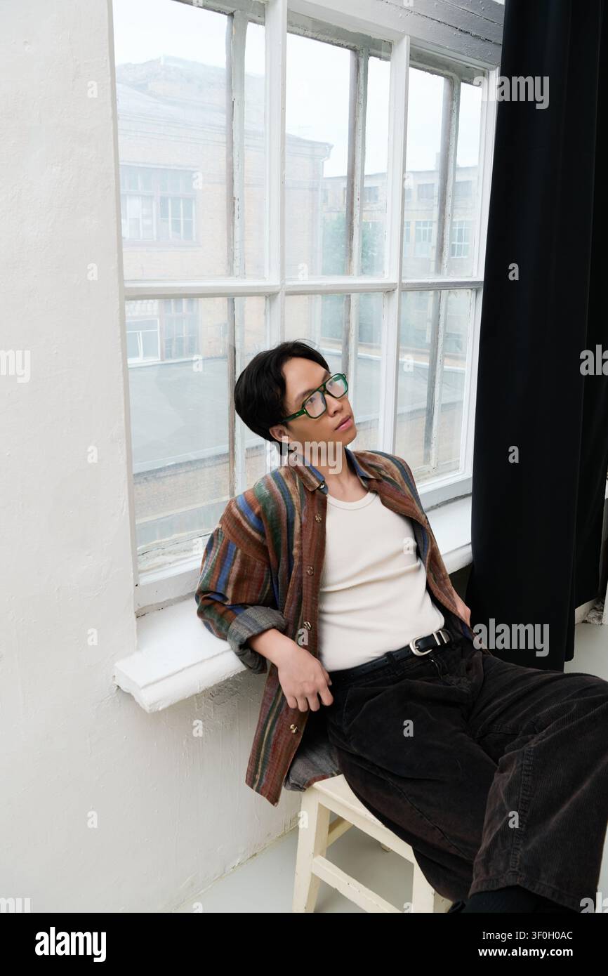 Ein junger, gutaussehender Asiate in eleganter Kleidung sitzt lässig und genießt den ruhigen Blick. Stockfoto