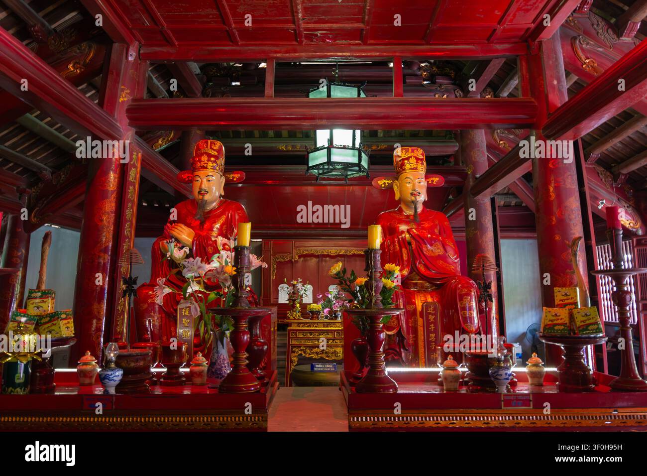 Konfuzius-Statuen im Literaturtempel in Hanoi mit traditionellen roten Holzsäulen und kunstvollen architektonischen Details Stockfoto
