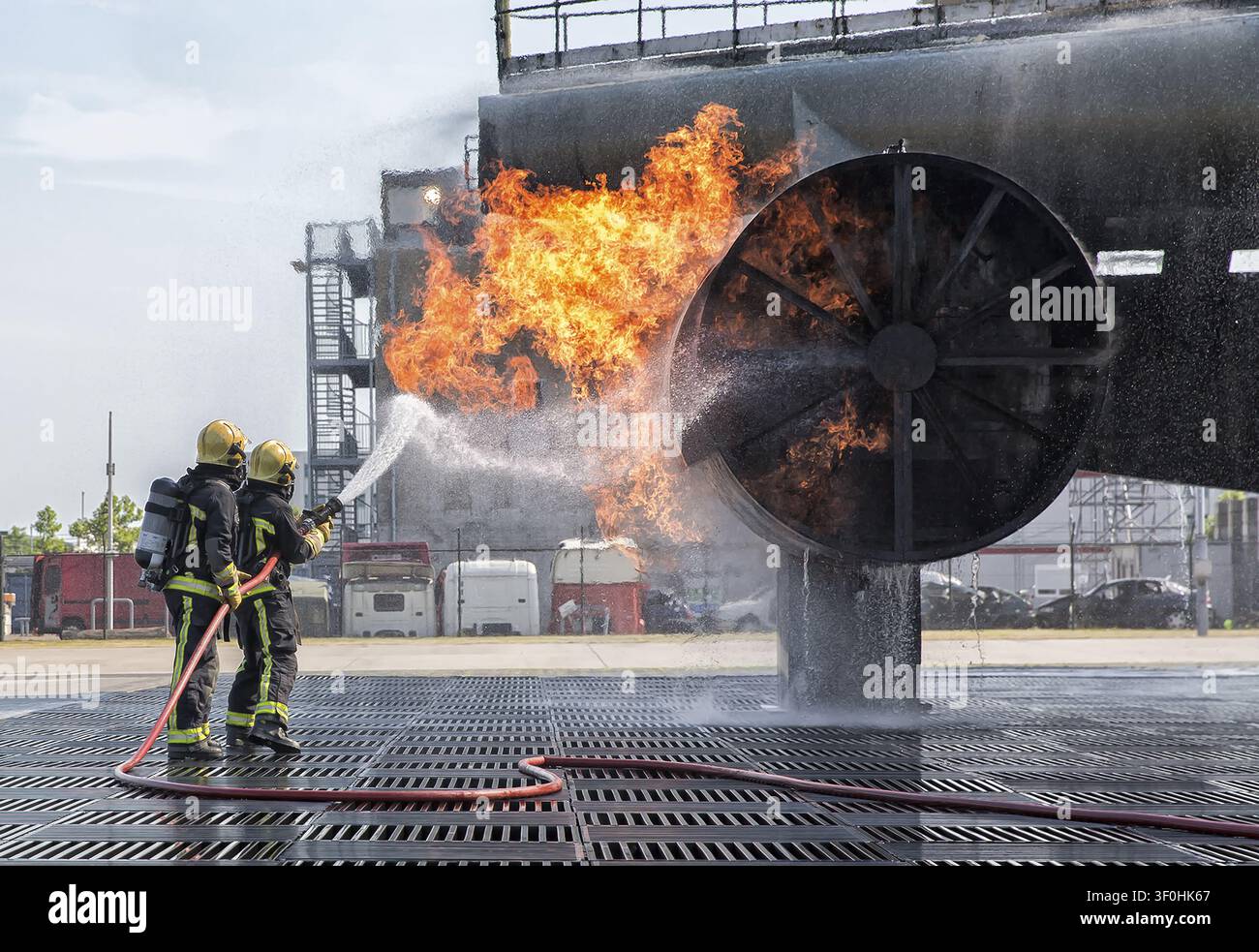 Ansicht von zwei Feuerwehrleuten in Schutzausrüstung, die mit einem Schlauch ein kontrolliertes Feuer an einer großen Metalltrainingsstruktur am Sloterweg 527 in Badho löschen Stockfoto