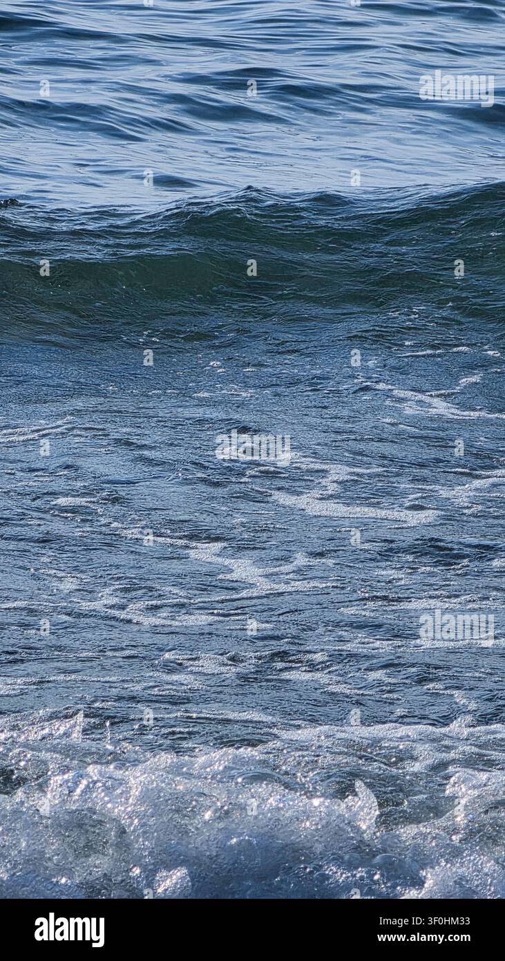 Detaillierte Nahaufnahme von sich bewegenden Meereswellen mit weißem Seeschaum und einer welligen Wasseroberfläche bei Tageslicht. Stockfoto