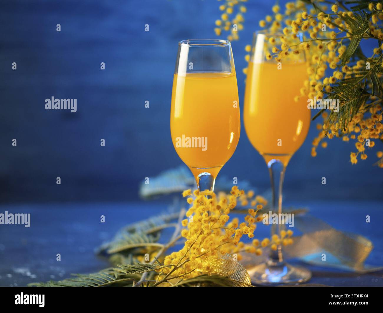 Mimosa-Cocktail mit Blumen auf blauem Hintergrund Stockfoto