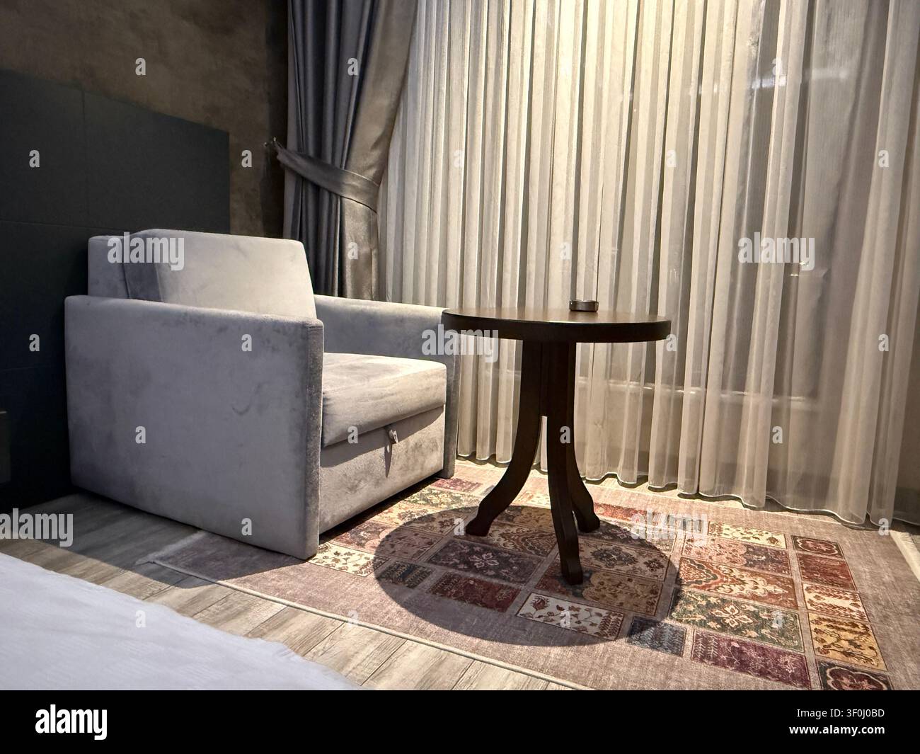 Gemütliche Wohnzimmerecke mit Sessel, rundem Tisch und eleganter Gardine als stilvoller Hintergrund. Mobilfoto Stockfoto