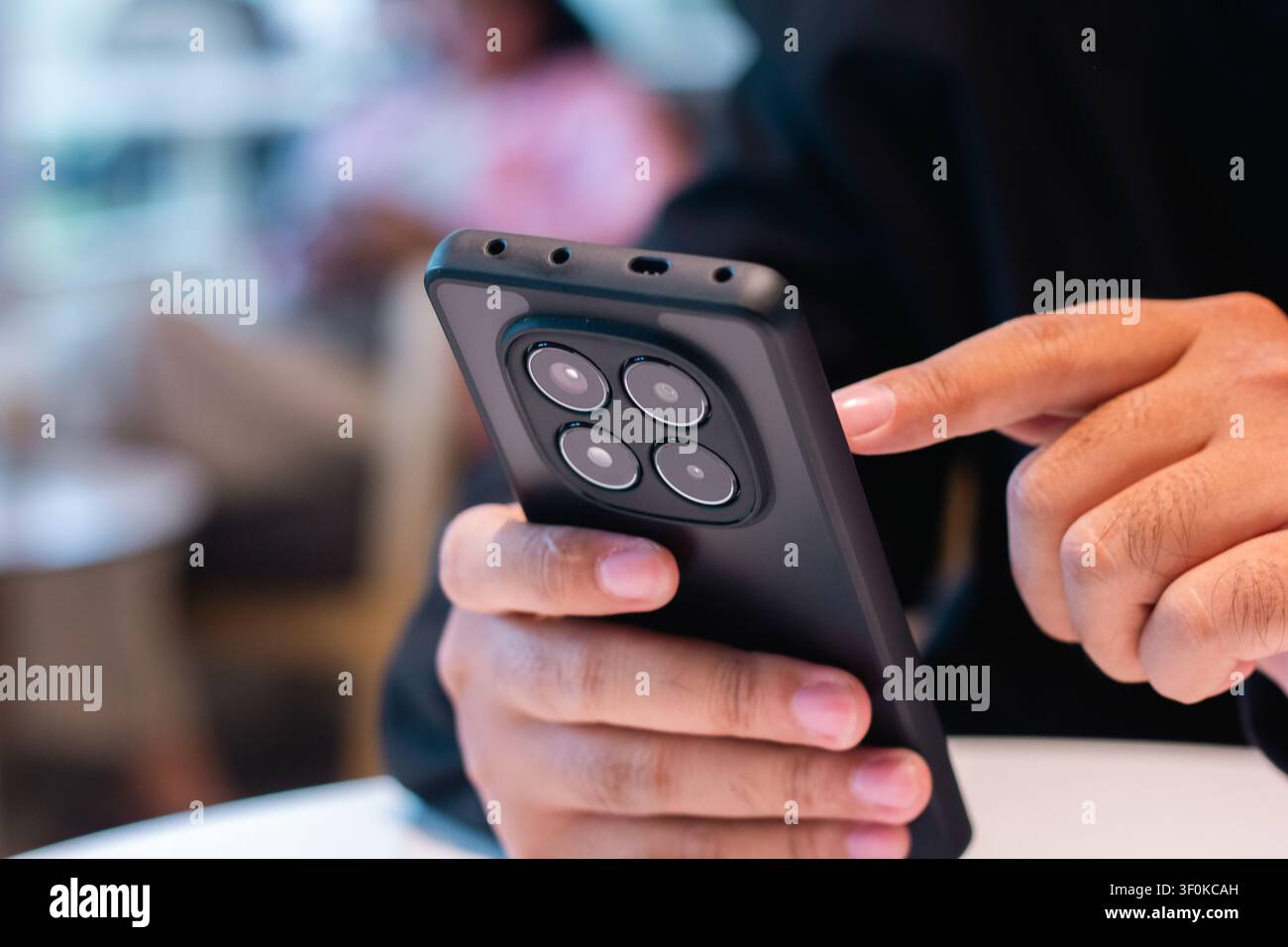 Eine Nahaufnahme eines Hands, das ein Mobilgerät hält, mit Fokus auf die Finger, die mit dem Touchscreen interagieren, und sanftem Innenlicht, das den Modus betont Stockfoto