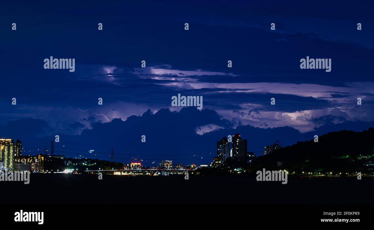 Ein dramatischer Nachtblick auf Tamsui, Neu-Taipeh, mit einem gewaltigen Gewitter, das die dunklen Wolken über der beleuchteten städtischen Skyline erhellt Stockfoto