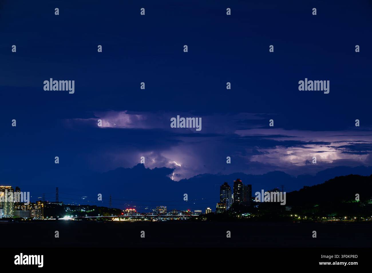 Ein dramatischer Nachtblick auf Tamsui, Neu-Taipeh, Taiwan, mit einem heftigen Gewitter, das die dunklen Wolken über der städtischen Skyline erhellt. Stockfoto
