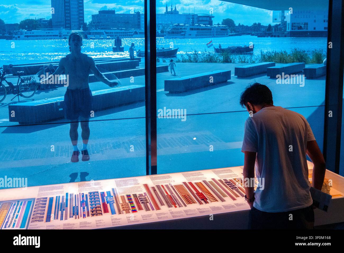 Mann, der vor den reflektierenden Fenstern des EYE Filmmuseums in Amsterdam, Holland, Niederlande, Europa hüpft Stockfoto