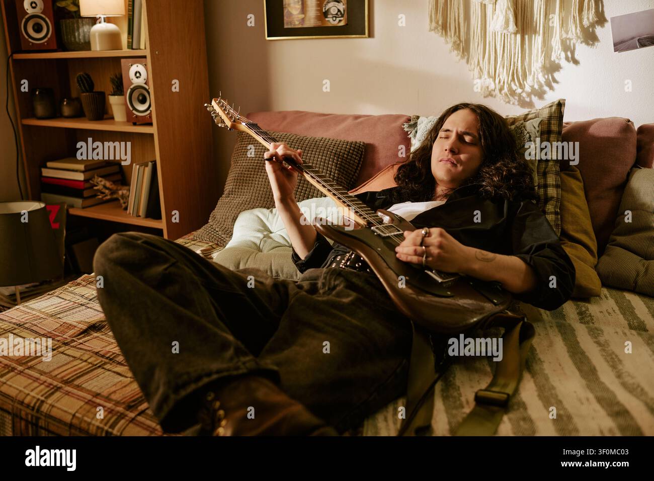 Langhaariger Mann spielt E-Gitarre zu Hause für den Musik-Lebensstil Stockfoto