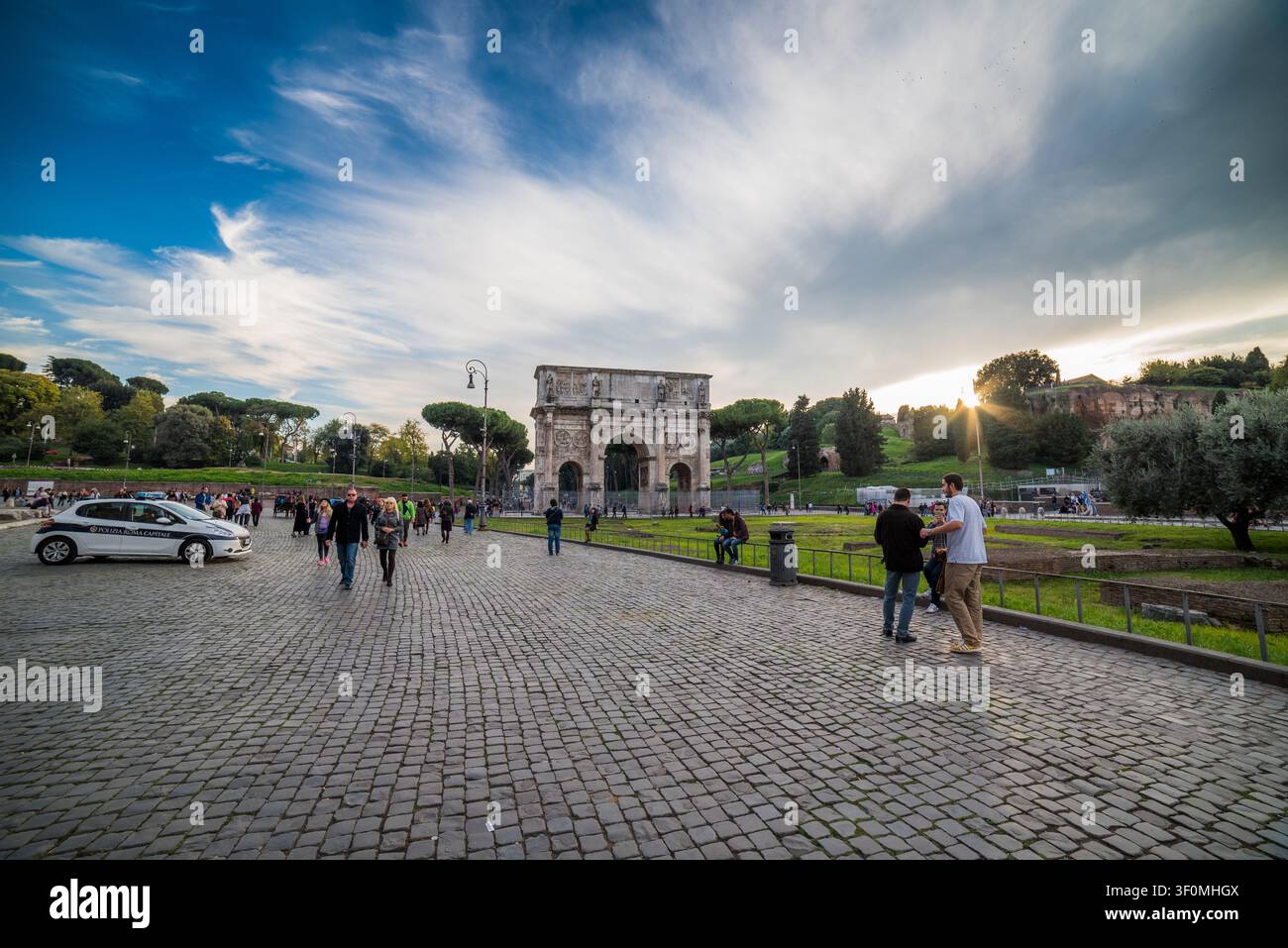 Touristen und ein Streifenwagen der Polizia Roma Capitale bevölkern den Kopfsteinpflasterplatz um den Konstantinsbogen in der Nähe des Kolosseums im alten Rom Stockfoto