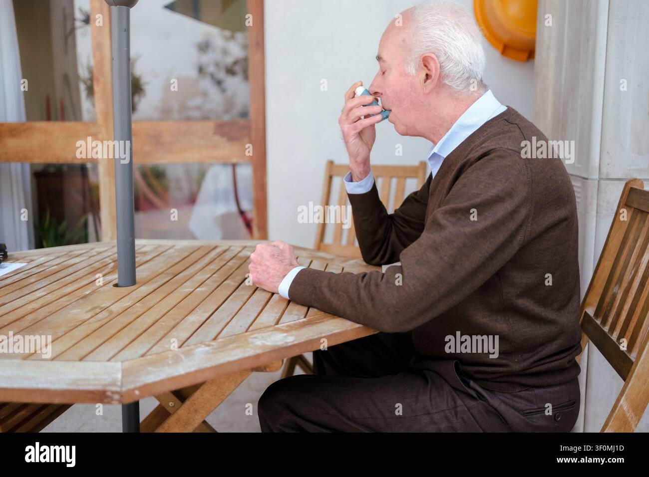 Senior Mann sitzt im Freien und verwendet ein Asthmaspray zum Atmen Stockfoto