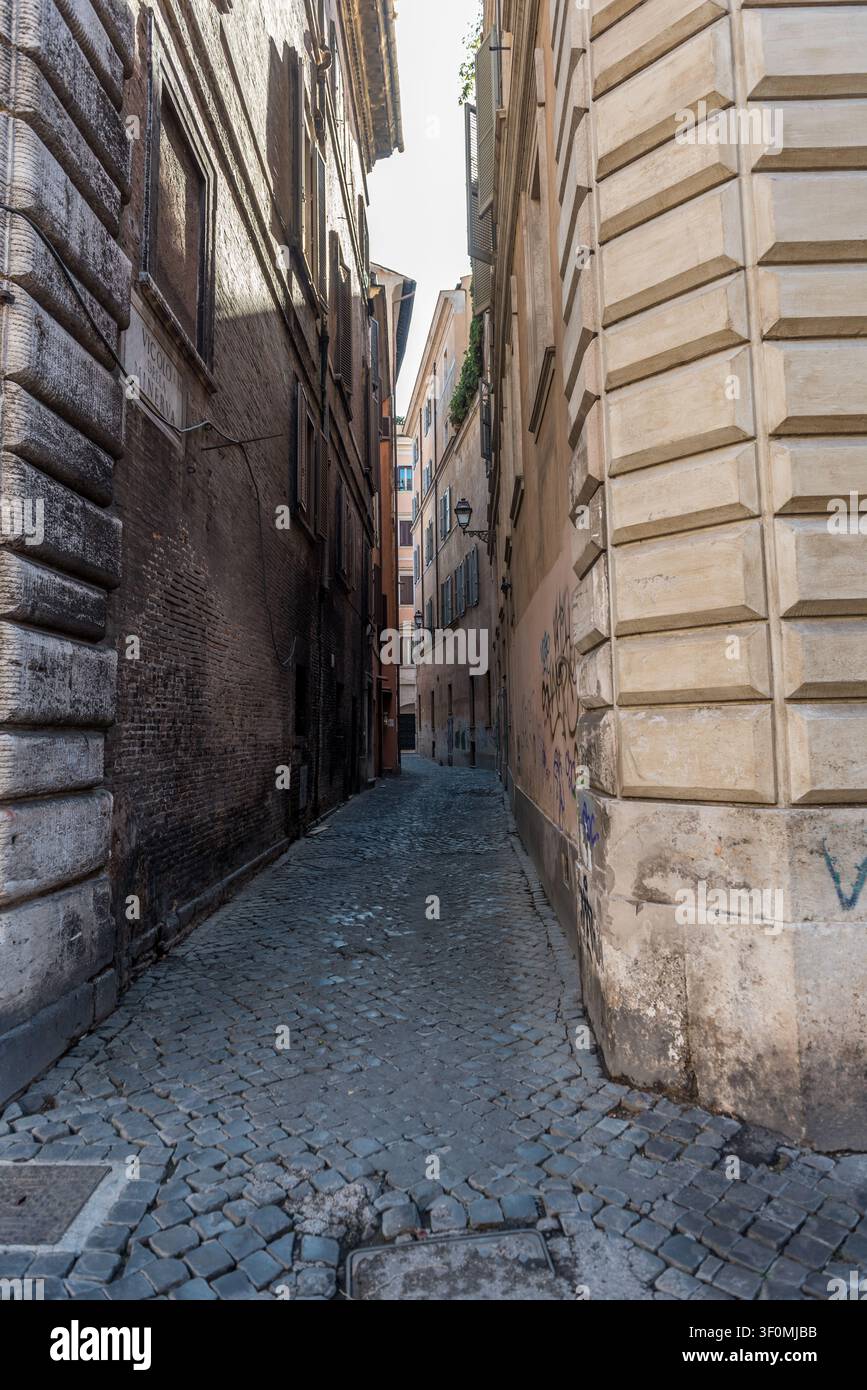 Ein schmaler mittelalterlicher Vicolo im Centro Storico von Rom, rechts flankiert von rustizierten Renaissance-Palazzo-Steinmetzarbeiten und gealterten Ziegelfassaden auf Stockfoto