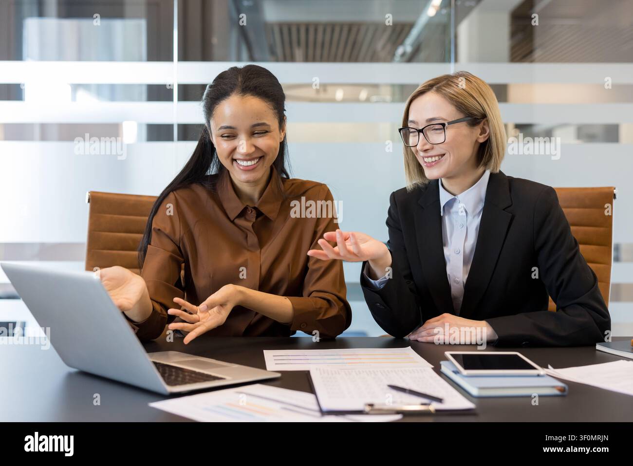 Verschiedene Geschäftsfrauen, die an einem Projekt zusammenarbeiten, aktiv Ideen diskutieren und eine positive Interaktion teilen, während sie zusammen an einem Konferenztisch in einem modernen Büroumfeld arbeiten Stockfoto