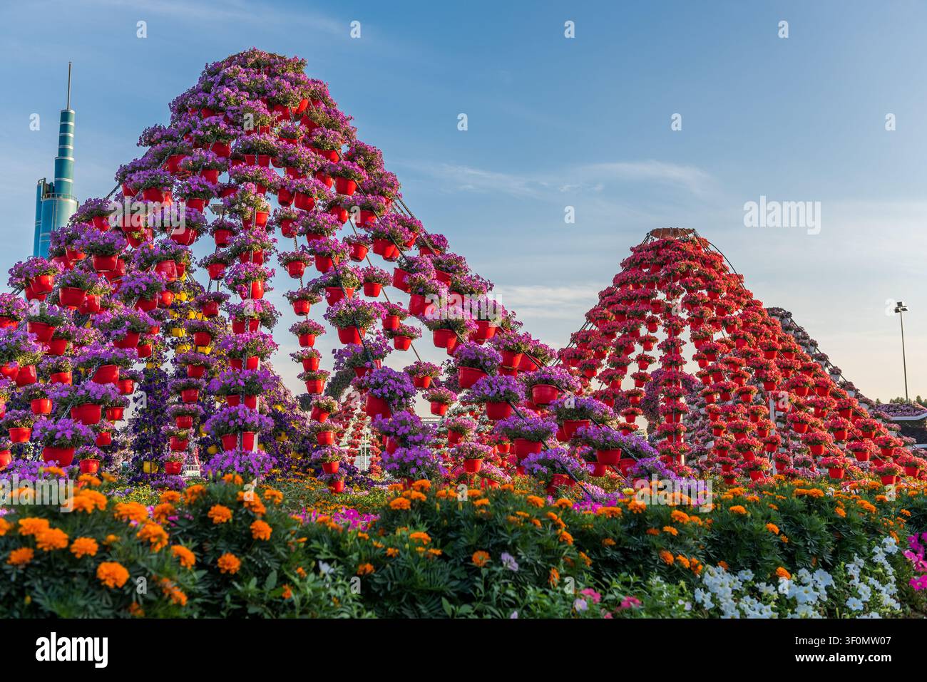 Turmhohe pyramidenförmige Blumeninstallationen, bedeckt mit Hunderten von roten hängenden Töpfen, die vor lila und rosa Petunien platzen, erheben sich über einen Vordergrund von Stockfoto