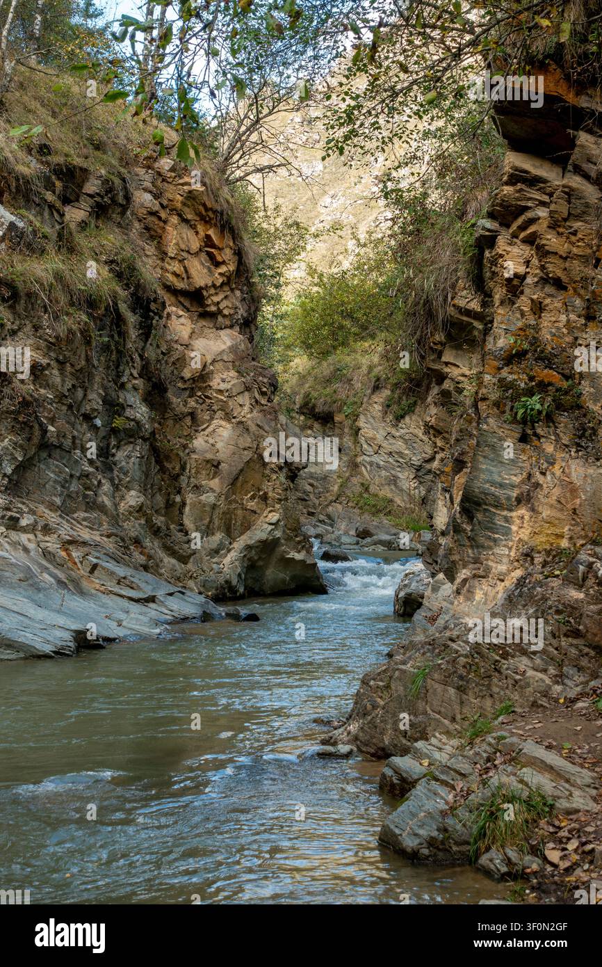 Eine enge felsige Schlucht leitet einen stürmischen Bergfluss zwischen hoch aufragenden geschichteten Sandstein- und Kalksteinhängen, die mit spärlicher Herbstvegetation bedeckt sind Stockfoto
