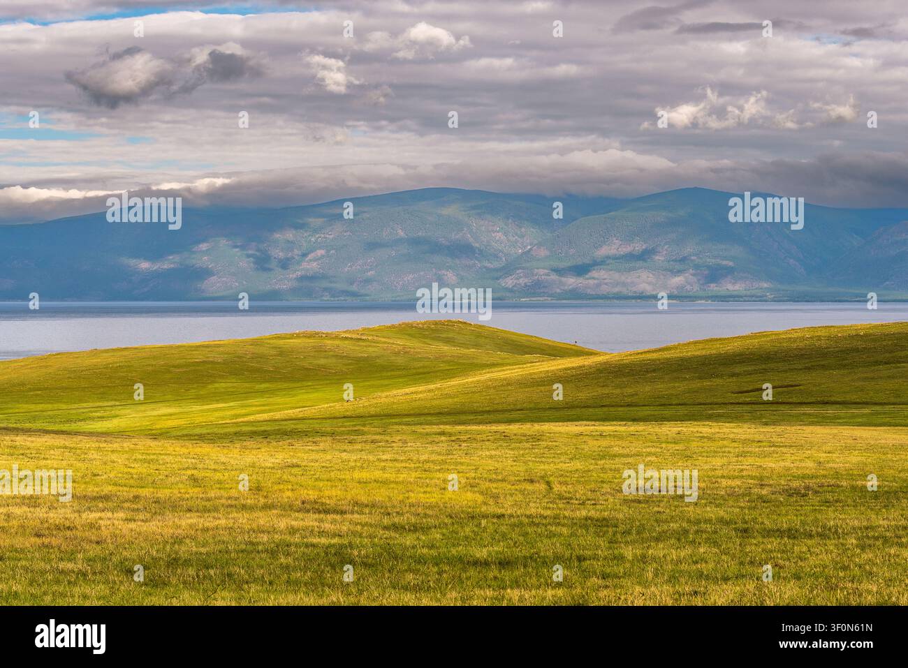 Rolle grüne Steppengründe ziehen sich hinab zu den ruhigen silbrigen Gewässern des Baikalsees. Stockfoto
