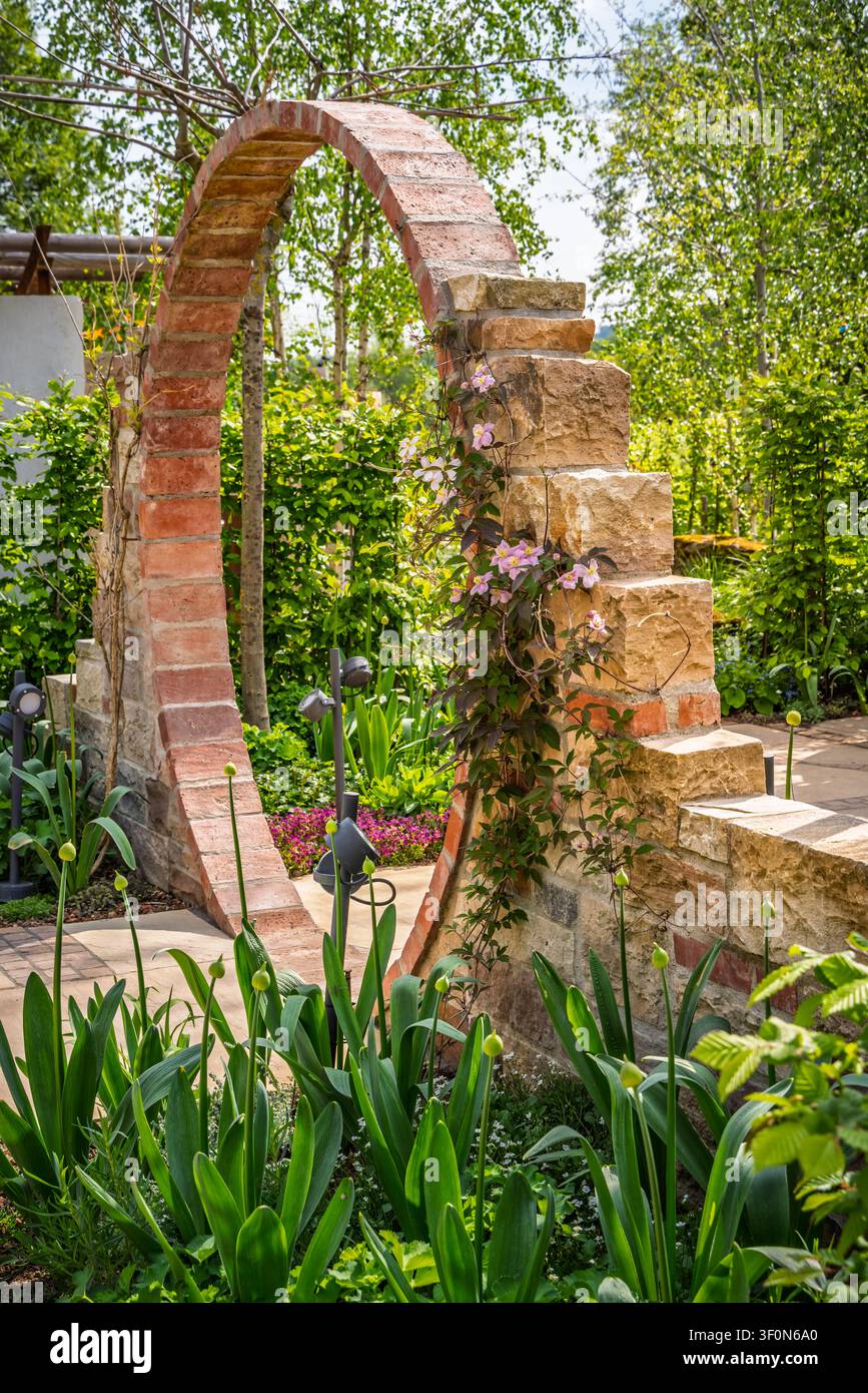 Charmanter Gartenbogen mit Kletterblumen und üppiger Vegetation Stockfoto