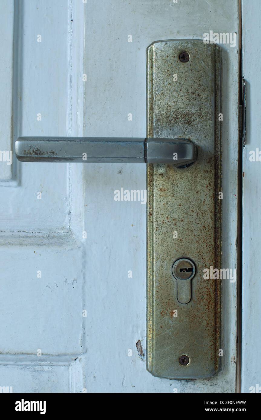 Nahaufnahme eines alten rostigen Metalltürgriffs und eines Schlosses mit Schlüsselloch an einer verwitterten weißen Holztür. Stockfoto