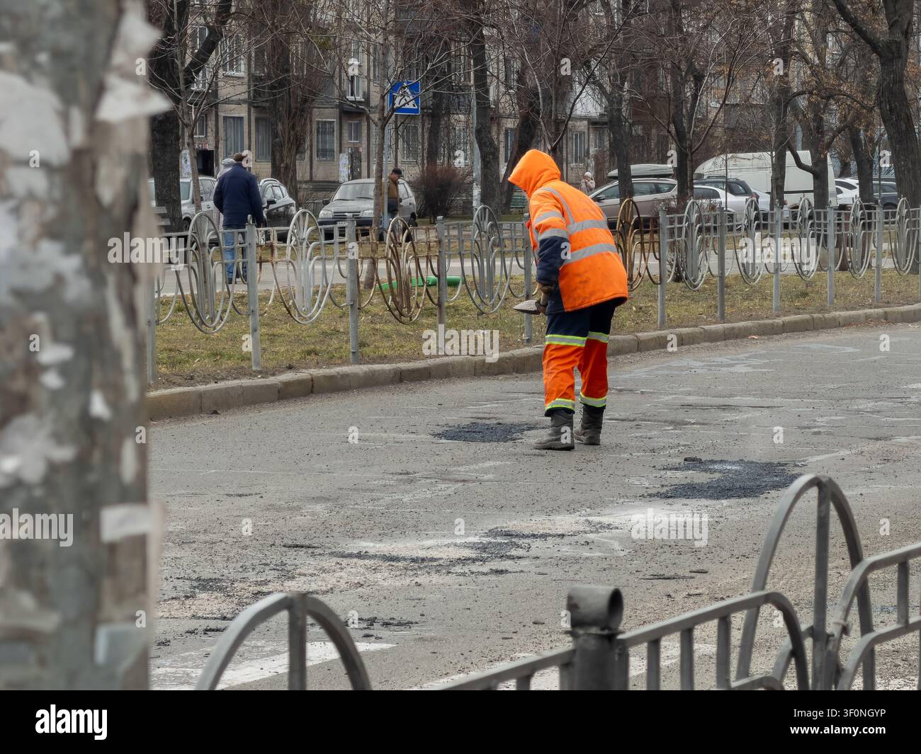 Ein Industriearbeiter verwendet ein Werkzeug, um Schlaglöcher auf einer Asphaltfläche zu flicken, und veranschaulicht damit städtische Erneuerungsbemühungen der Gemeinde, die funktionale Tra… Stockfoto