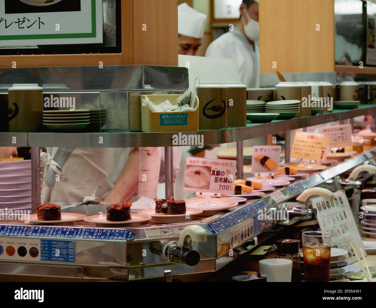 Sushi-Teller auf einem Förderband in einem Kaiten-Zushi-Restaurant mit Köchen, die hinter der Theke arbeiten, Shibuya, Tokio, Japan Stockfoto