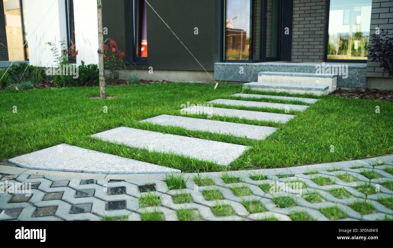 Garten eines modernen Hauses mit einem Weg aus rechteckigen Steinplatten auf lebhaftem grünem Rasen, der zu den Eingangsstufen führt Stockfoto