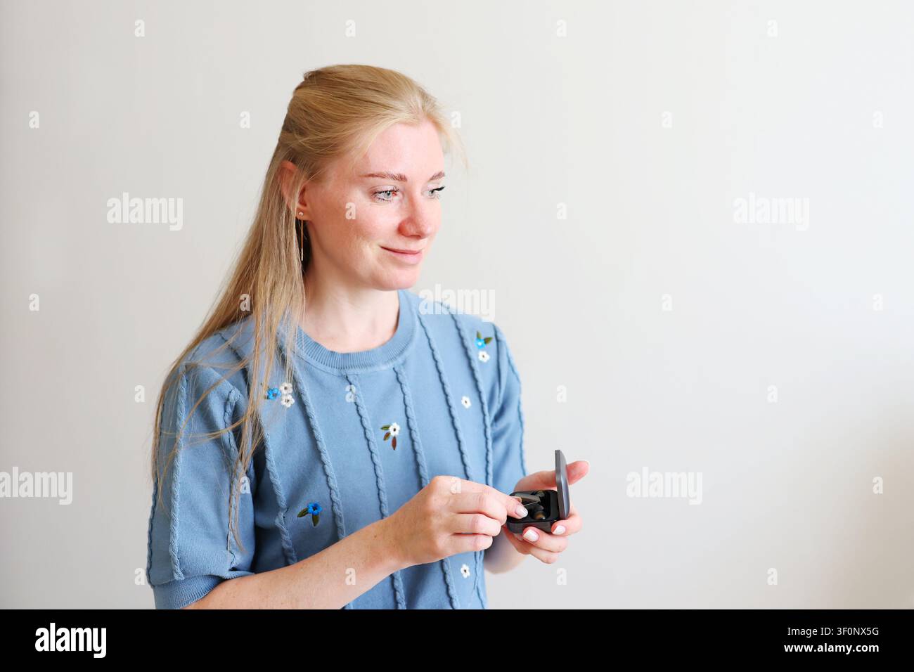 Junge Frau, die kabellose Ohrhörer anlegt, bevor sie Musik hört, einen Podcast abhört oder an einem Online-Anruf teilnimmt zu Hause. Stockfoto