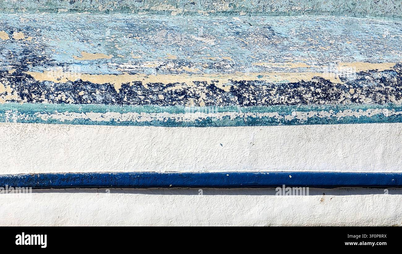 Nahaufnahme einer verwitterten Wand mit abblätternder blauer, weißer und beiger Farbe, texturierten Schichten und Rissen, die rustikale und gealterte Oberflächendetails zeigen Stockfoto