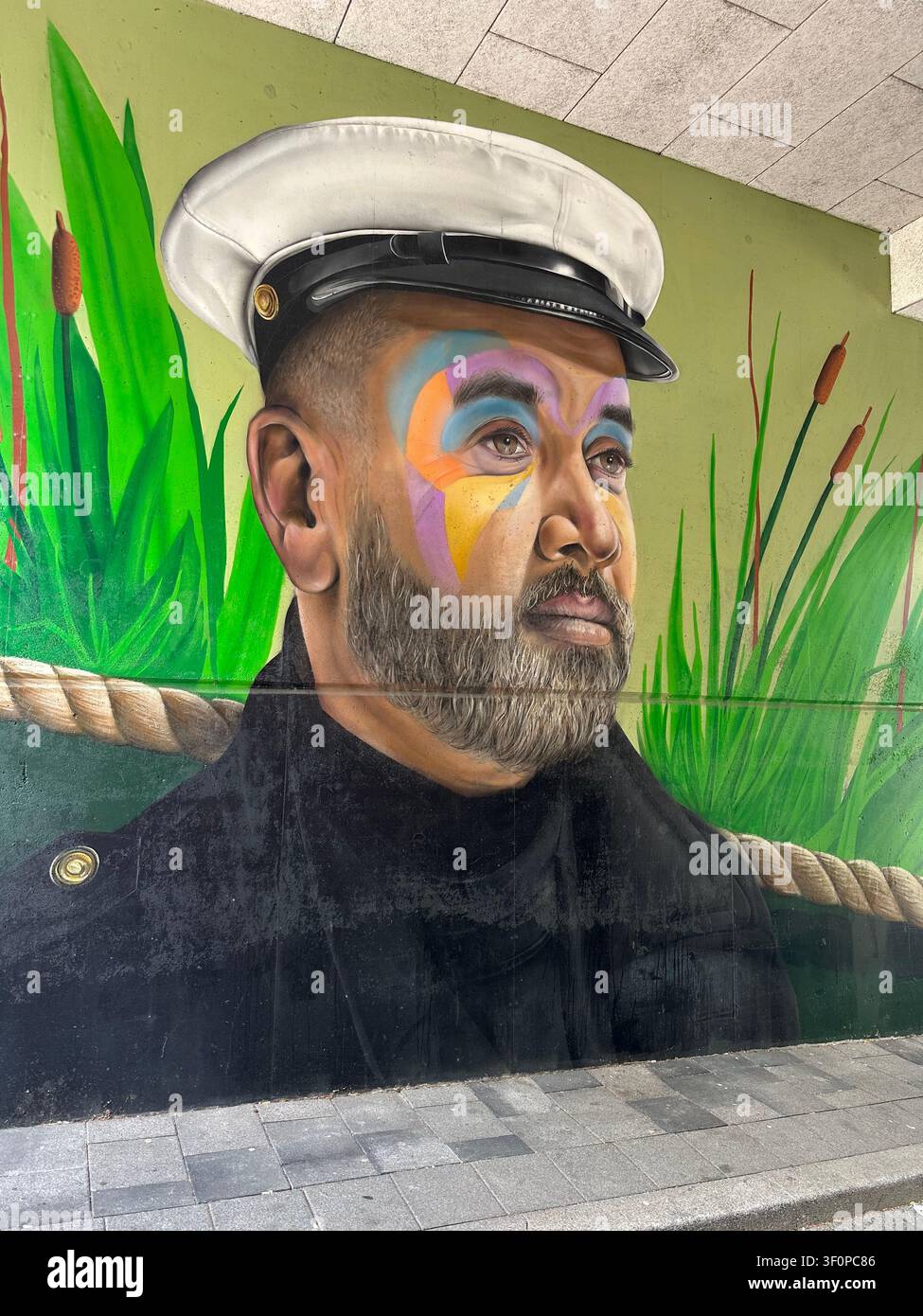 Farbenfrohes Straßenkunst-Mural eines Mannes mit Kapitänsmütze und kreativem Make-up. Lebendige Graffiti-Malerei an einer Außenwand, die einen bärtigen Matrosen darstellt - Smartphone-aufgenommenes Stockfoto