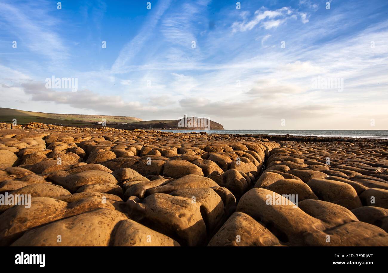 Niedrigwinkelaufnahme von durch Meerwasser erodierten Felsen in Kimmeridge Bay Dorset UK mit Blick auf den Clavel Tower unter einem dramatischen Küstenhimmel Stockfoto