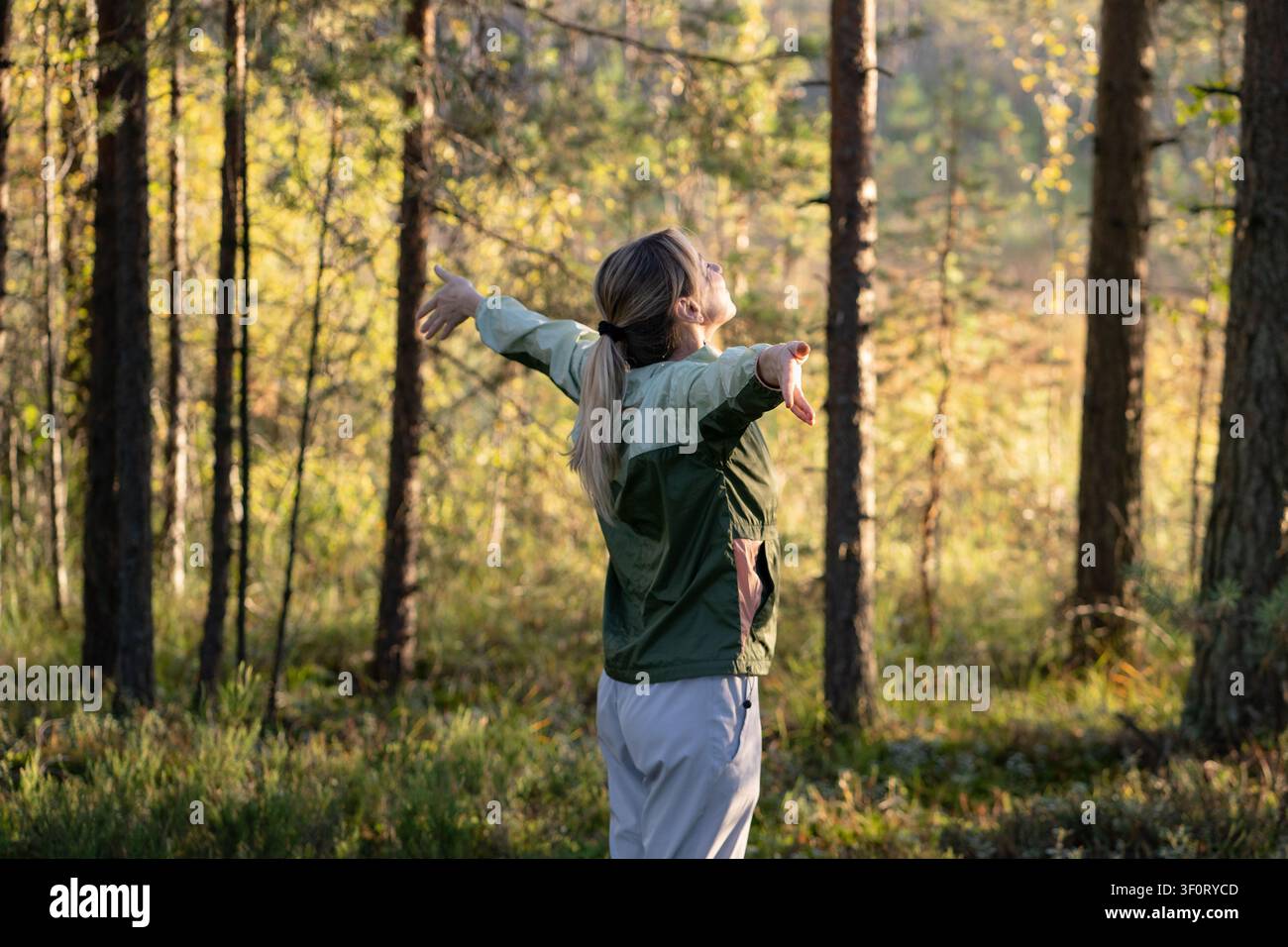 Fröhliche Frau, die die Natur auf einem Waldspaziergang umarmt, mit ausgebreiteten Armen stehend und frische Luft einatmend. Stockfoto