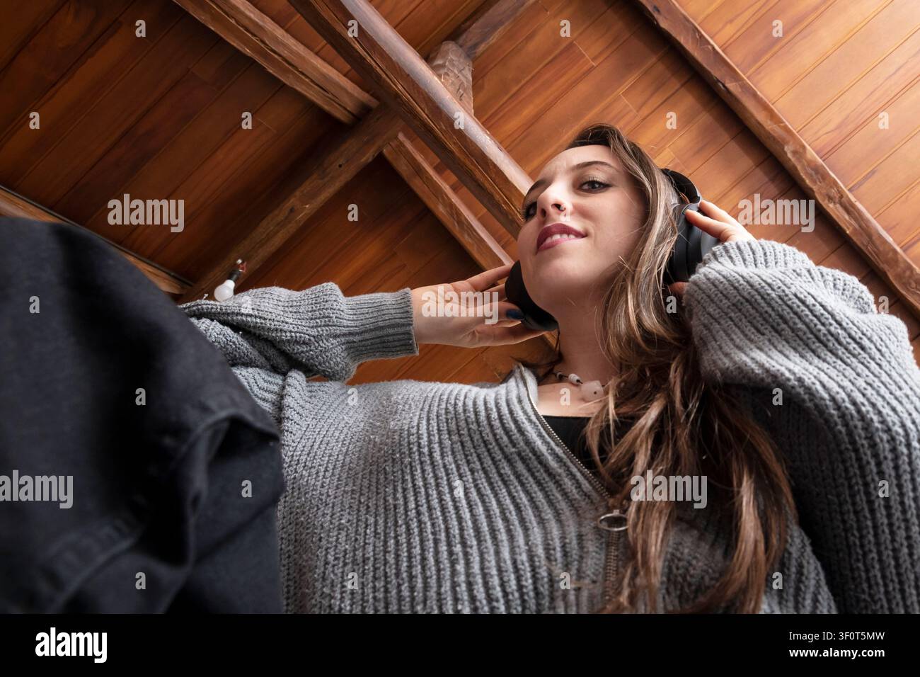 Niedrigwinklige Ansicht einer jungen Frau, die drinnen Musik mit kabellosen Kopfhörern genießt Stockfoto