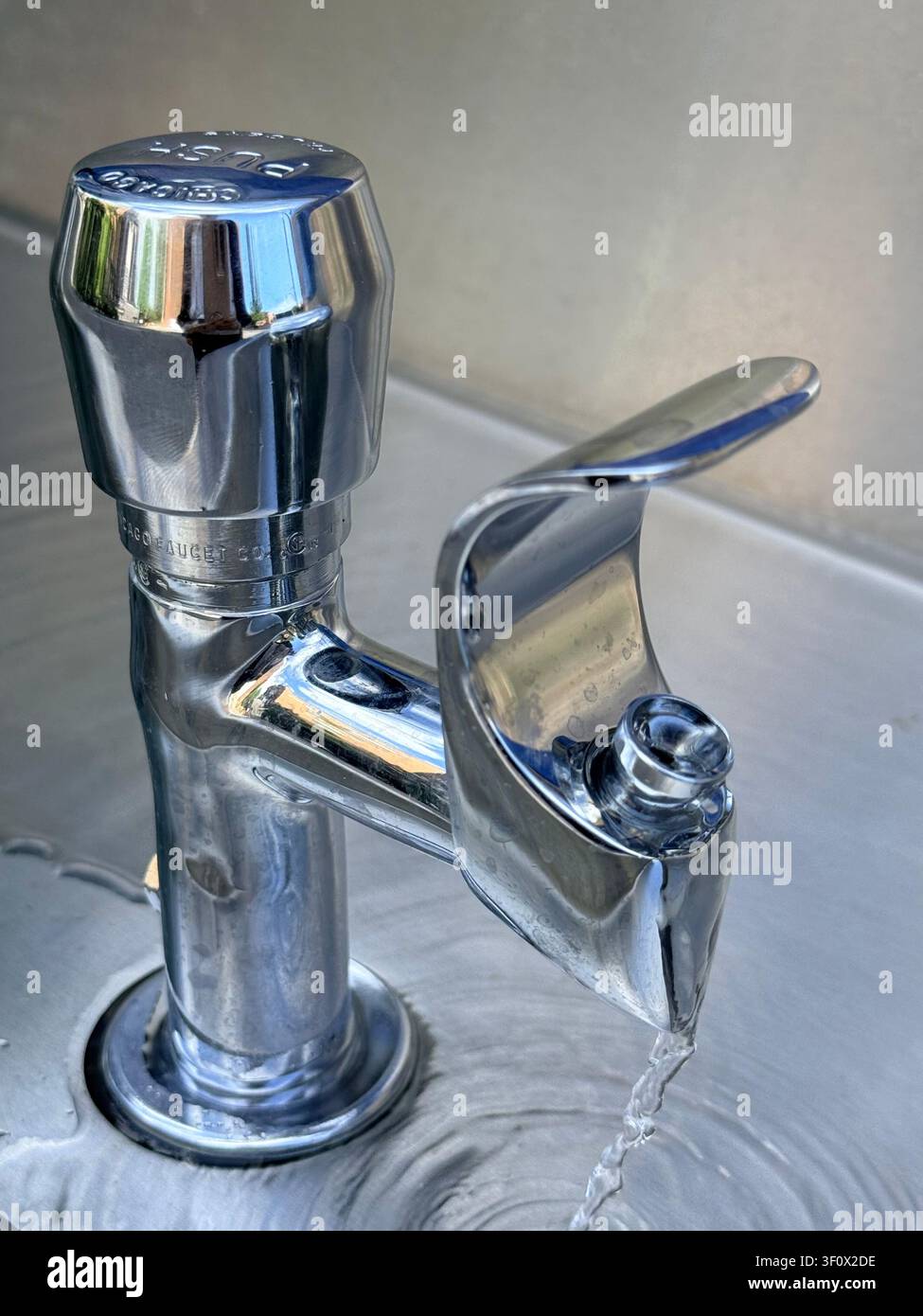 Nahaufnahme von Leitungswasser, das aus einem Chrom-Wasserhahn in ein Edelstahl-Spülbecken fließt, illustriert die Nutzung von Trinkwasser, den Wasserverbrauch und die Wassermangel. Stockfoto