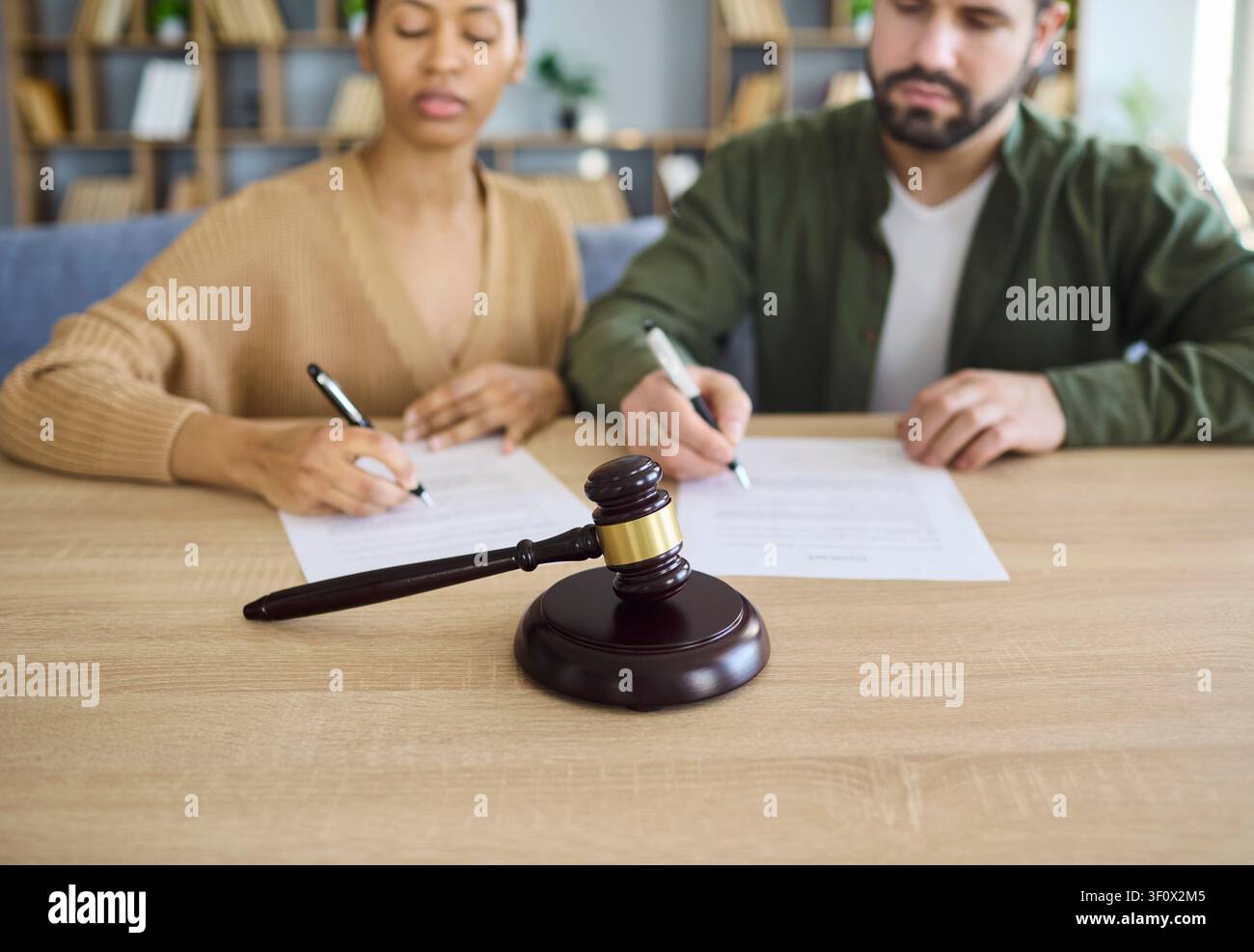 Paar unterzeichnet Scheidungspapiere am Schreibtisch mit Gerichtshammer, Trennungskonzept Stockfoto