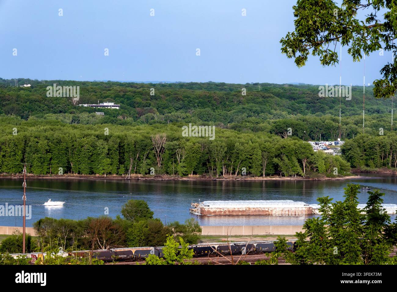 Dubuque, Iowa, USA - 16. Mai 2026: Frachtkahn fährt entlang des Mississippi an bewaldeten Klippen in der Nähe von Dubuque, Iowa, an einem ruhigen Sommerabend Stockfoto