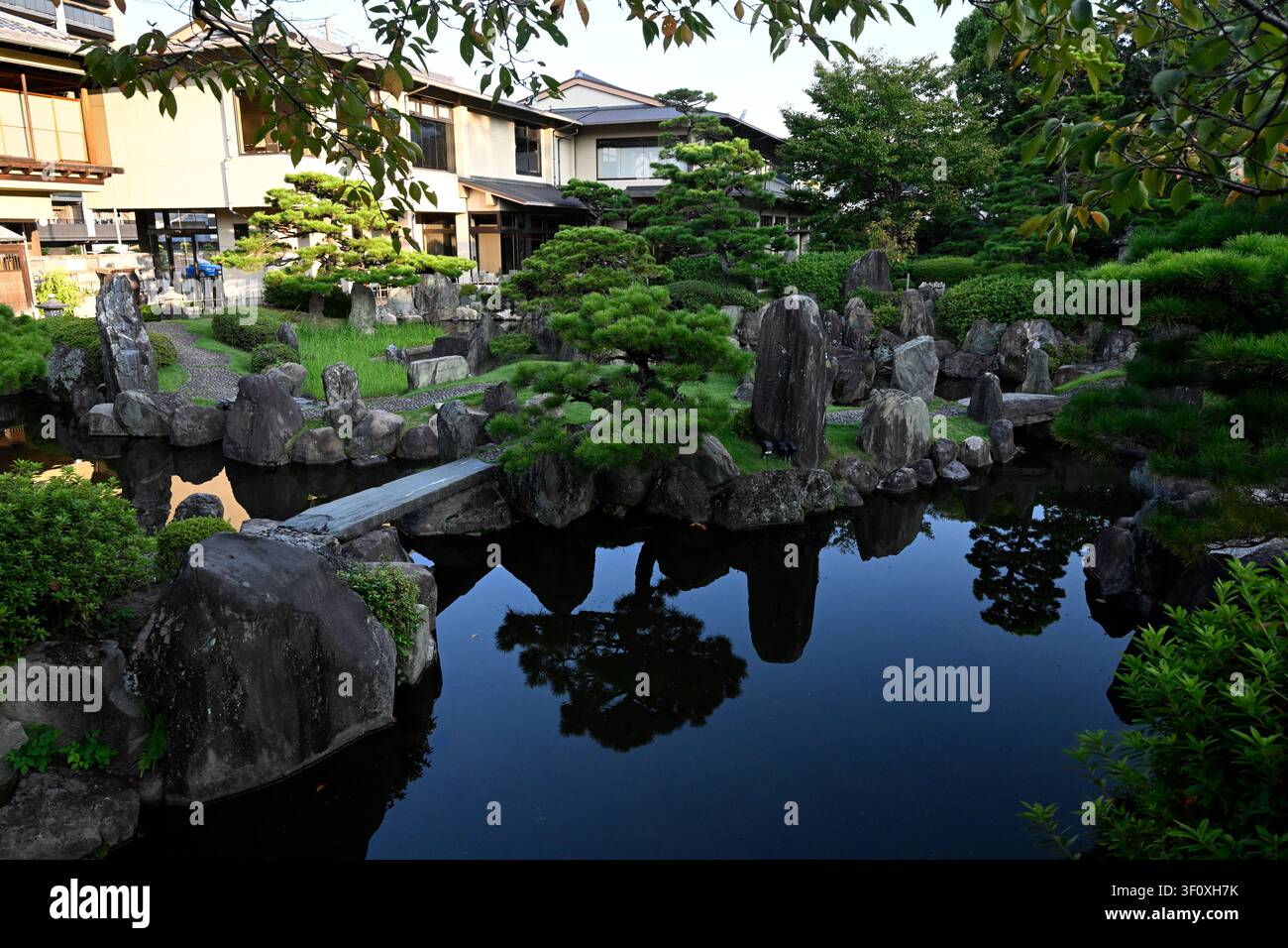 Traditioneller japanischer Teichgarten mit beschnittenen Kiefern, monumentalen Steinen, spiegelndem Wasser und einer Steinbrücke im Hanbe-Garten, einem exklusiven Ka Stockfoto