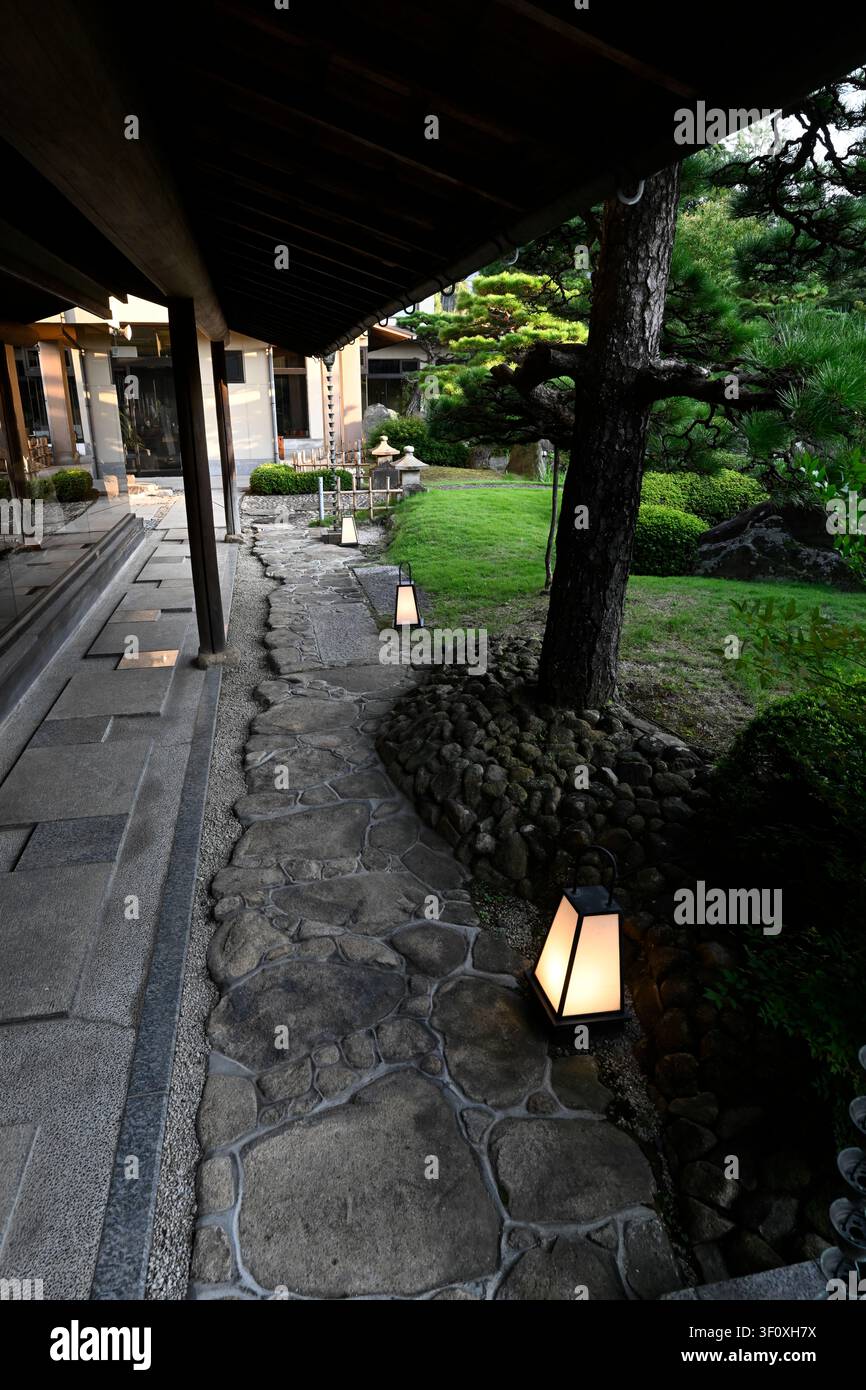 Ein traditioneller Steinpfad, der von Laternen beleuchtet wird, windet sich durch die Gärten des Hanbe Garden, dem historischen Kaiseki-Restaurant in Hiroshima, Japan. Co Stockfoto