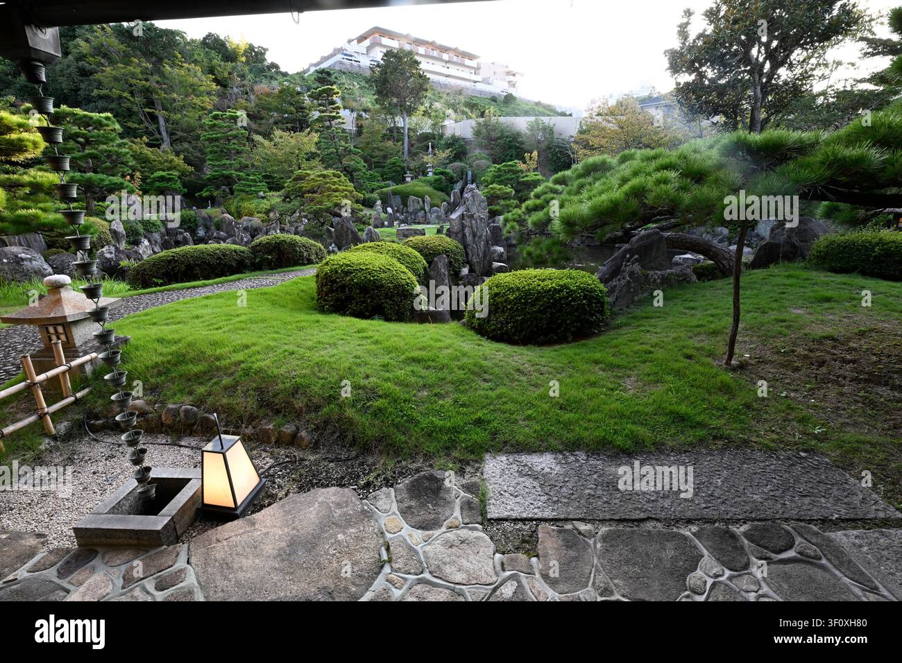 Blick von der überdachten Veranda über den gestalteten Teichgarten im Hanbe-Garten, einem historischen Kaiseki-Restaurant in Hiroshima, Japan. Gebildete Kiefer Stockfoto