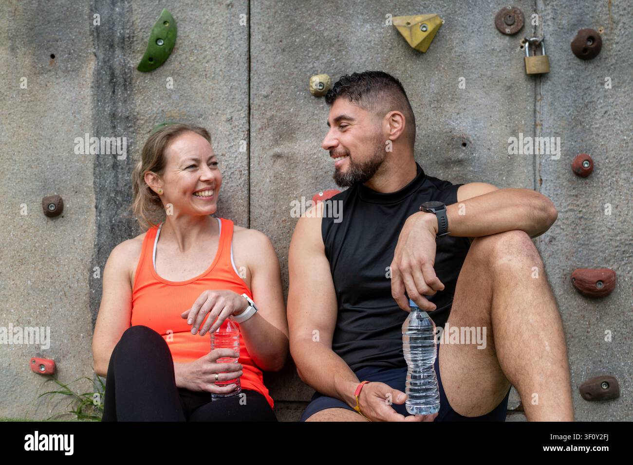 Glückliches sportliches Paar ruht sich nach dem Training aus und trinkt Wasser im Freien Stockfoto
