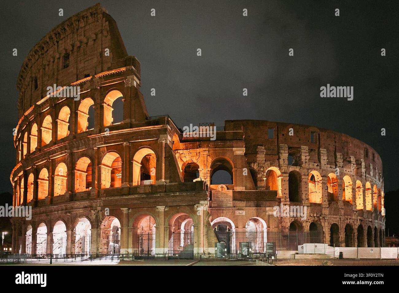 Nachtansicht des Kolosseums in Rom, Italien, mit dramatischer architektonischer Beleuchtung, die seine mehrstufigen Bögen, die Travertinfassade und Anc Stockfoto