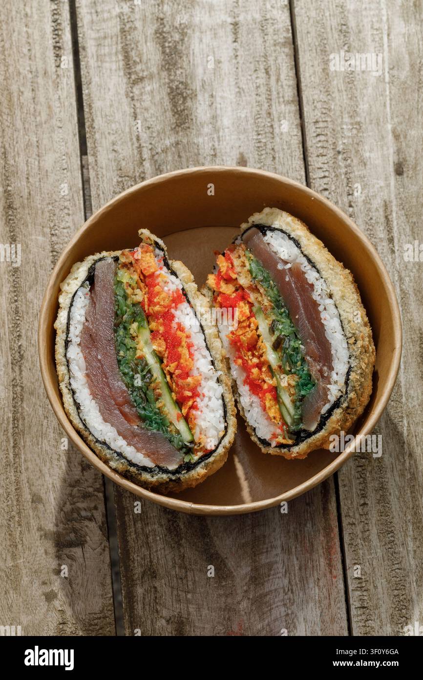 Sushi-Burger in einer Lieferbox auf einem Holz-Hintergrund. Isoliert. Kunstvolles Foto. Professionelle Studiolichttechnik. Stockfoto