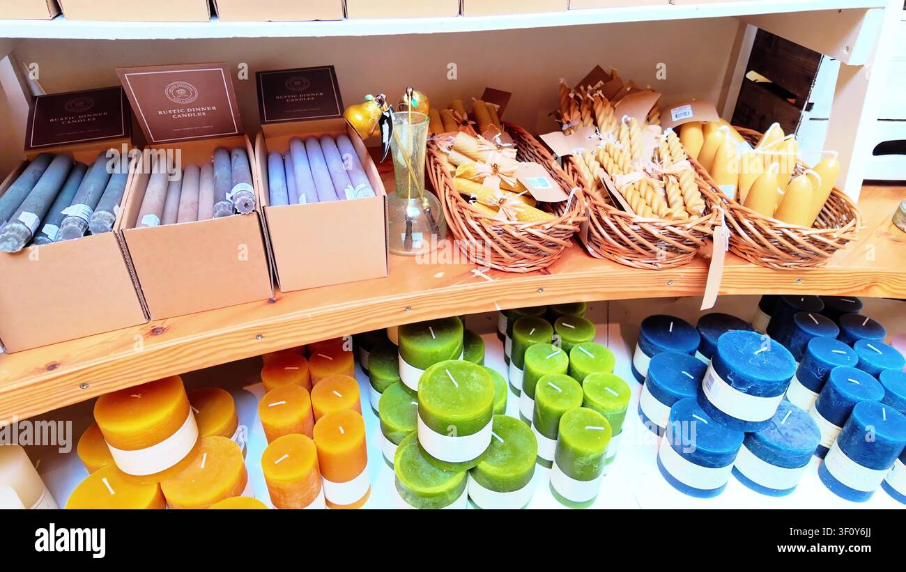 Ladenauslage einer Farm mit bunten handgefertigten Bienenwachskerzen, Abendkerzen und gewebten Körben auf Holzregalen Stockfoto