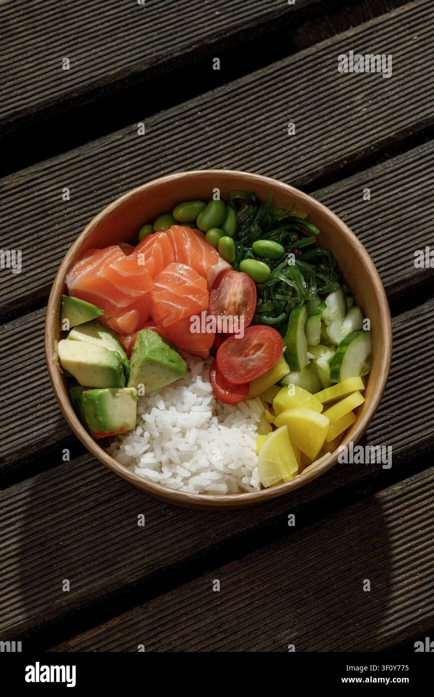 Lachs-Poke-Schüssel in einer Lieferbox auf einer Holzoberfläche. Isoliert. Platz für Text. Professionelle Studiolichttechnik. Stockfoto