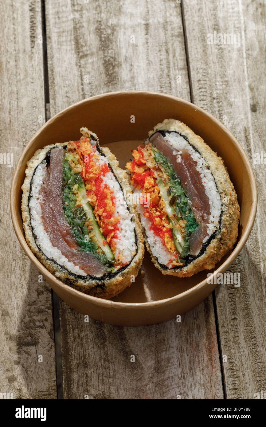 Sushi-Burger in einer Lieferbox auf einem Holz-Hintergrund. Isoliert. Kunstvolles Foto. Professionelle Studiolichttechnik. Stockfoto