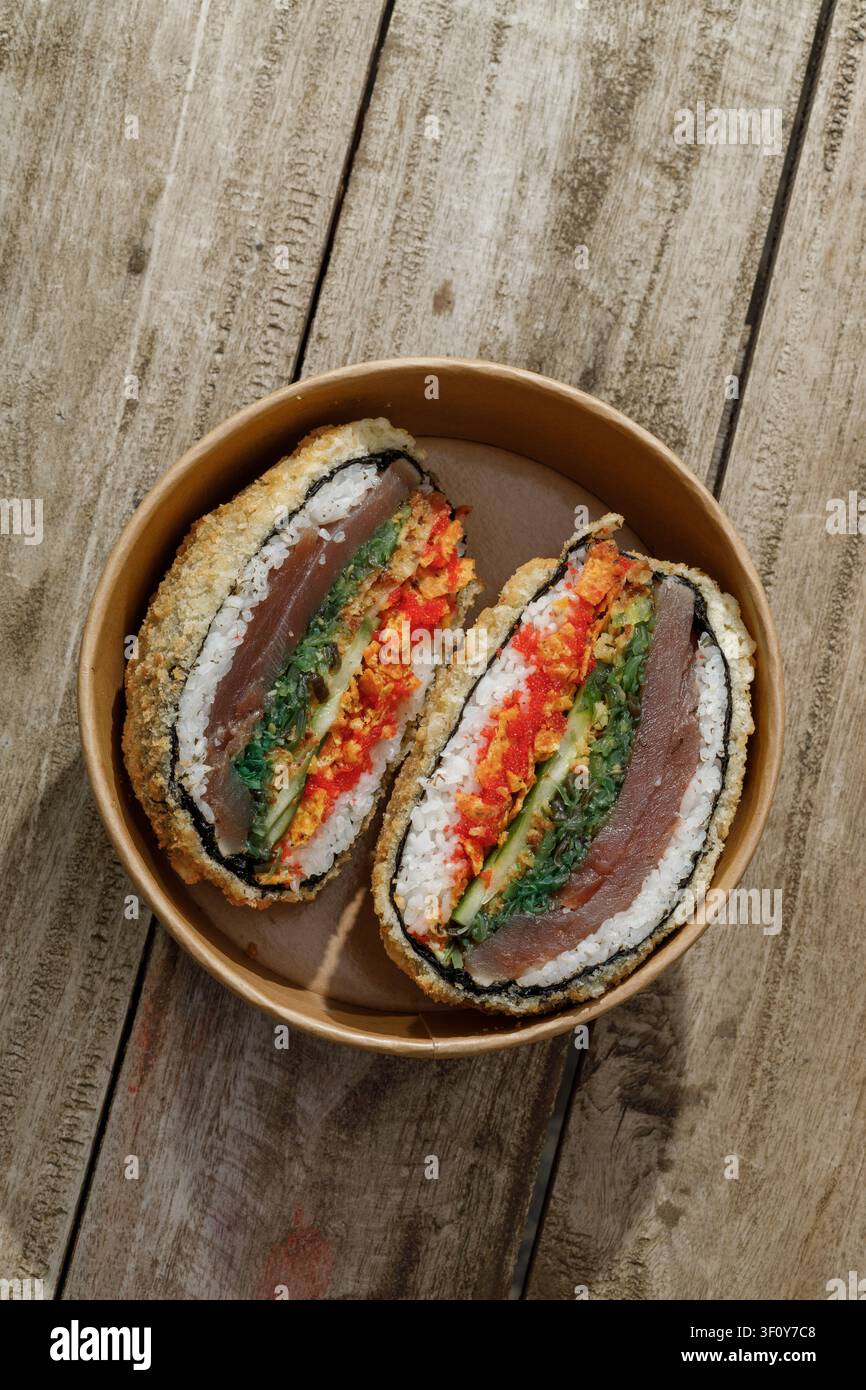 Sushi-Burger in einer Lieferbox auf einem Holz-Hintergrund. Isoliert. Kunstvolles Foto. Professionelle Studiolichttechnik. Stockfoto