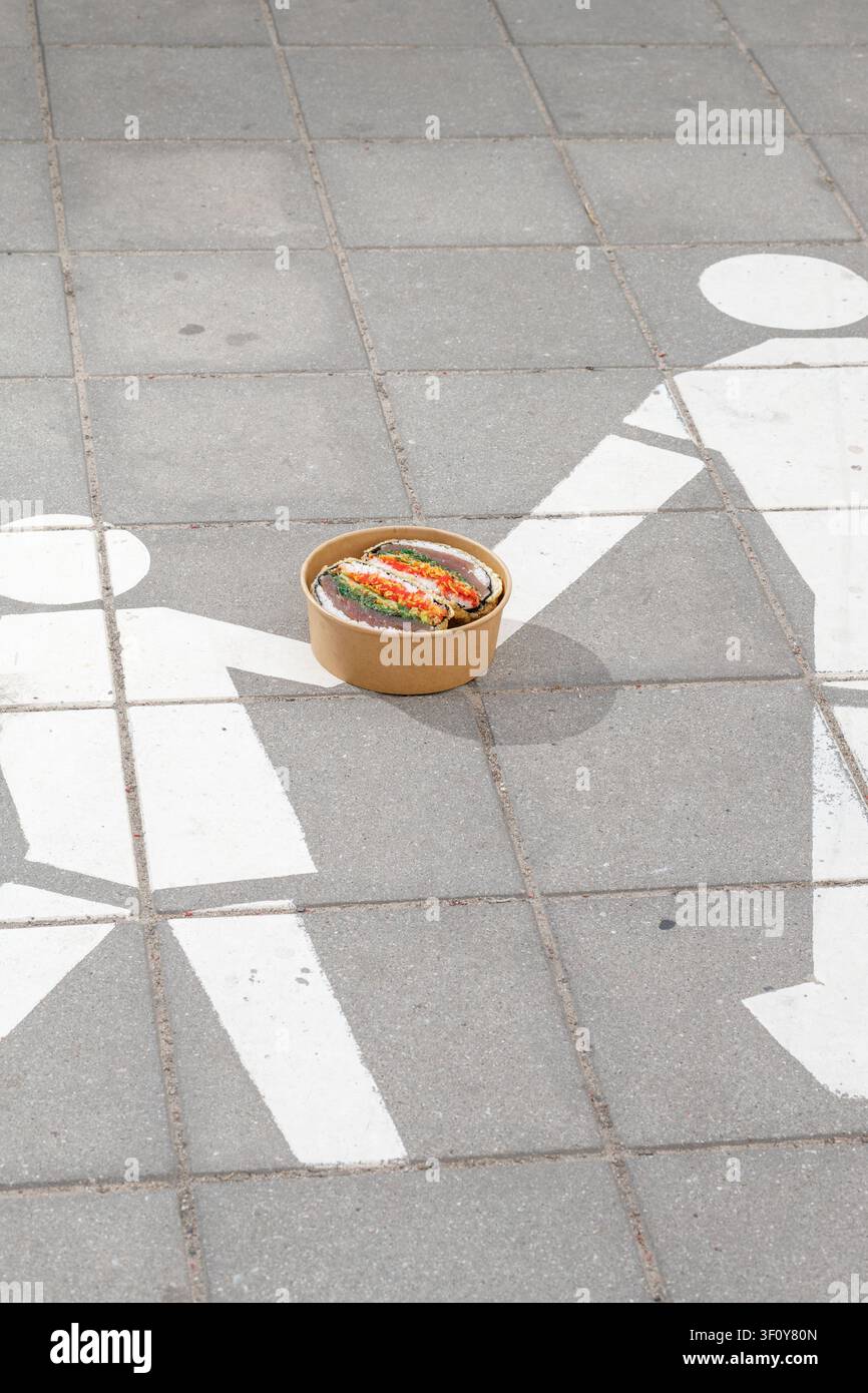 Sushi-Burger in einer Lieferbox vor dem Hintergrund eines "Fußgängerzone“-Schildes. Kreative Kunst. Isoliert. Platz für Text. Stockfoto