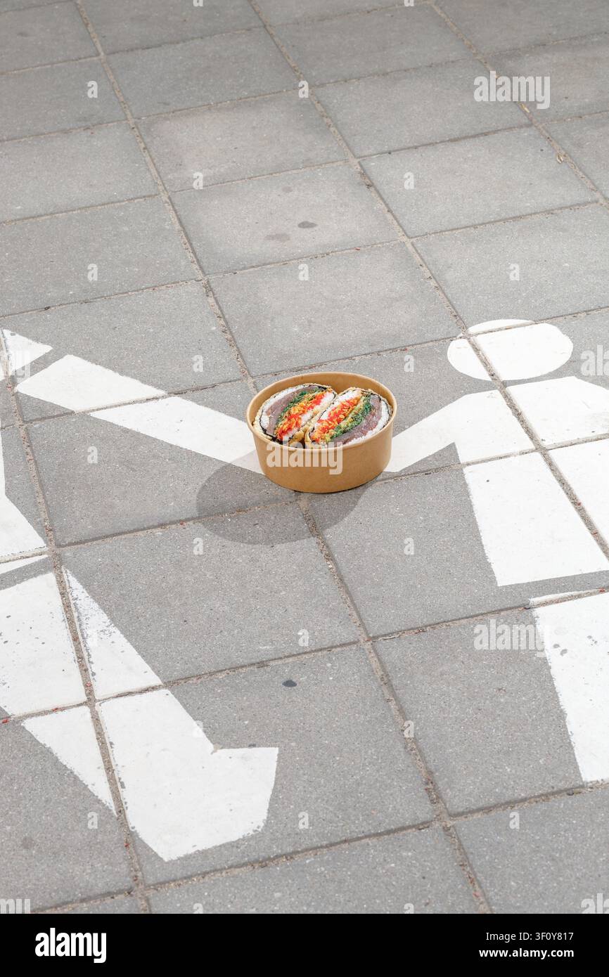Sushi-Burger in einer Lieferbox vor dem Hintergrund eines "Fußgängerzone“-Schildes. Kreative Kunst. Isoliert. Platz für Text. Stockfoto