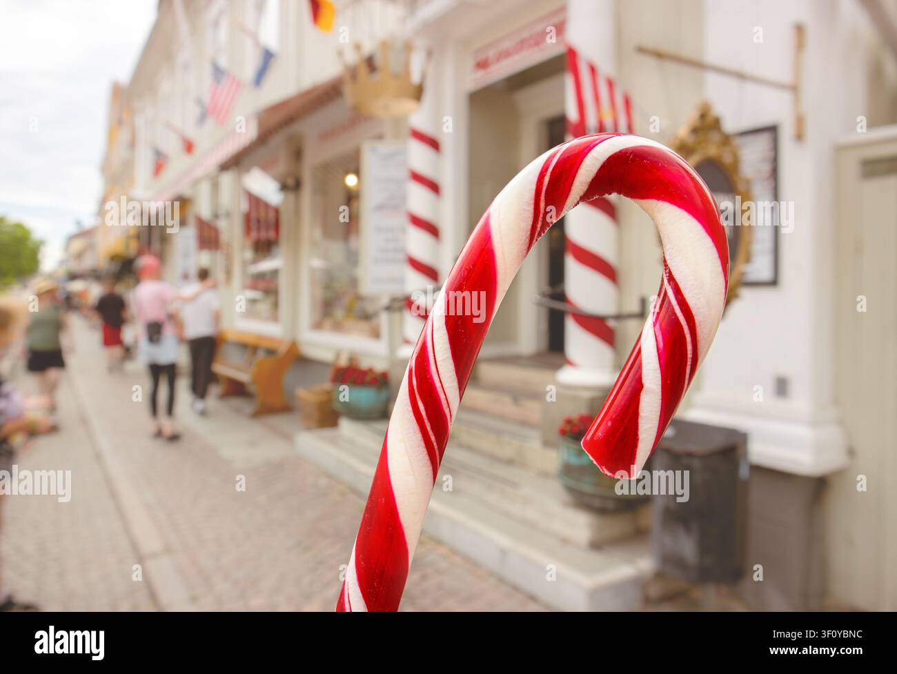 Nahaufnahme einer Touristenhand, die rote und weiße Polkagris, schwedischen Stockzucker, hält, mit unscharfem Hintergrund der Stadt Gränna in Schweden. Stockfoto