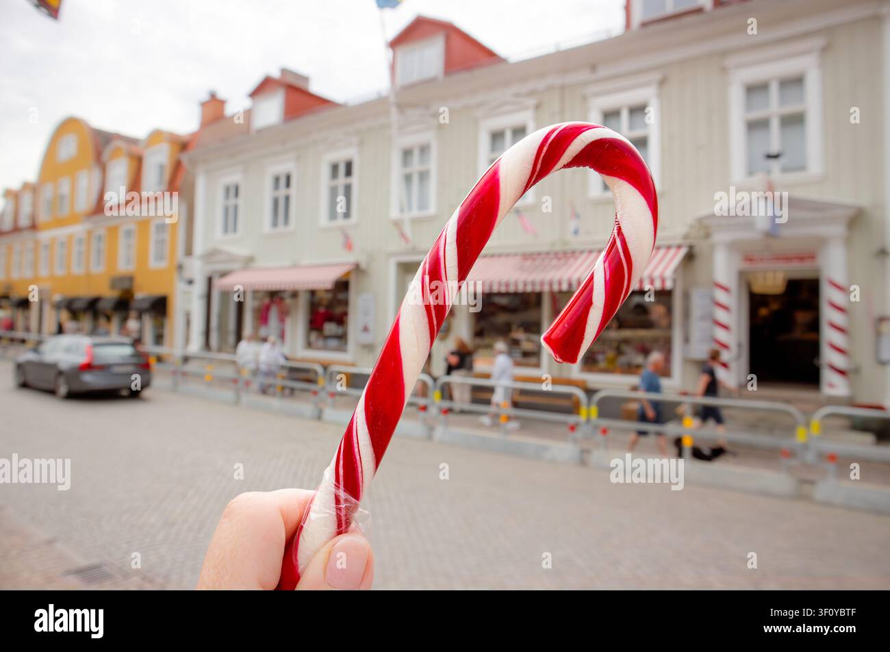 Nahaufnahme einer Touristenhand, die rote und weiße Polkagris, schwedischen Stockzucker, hält, mit unscharfem Hintergrund der Stadt Gränna in Schweden. Stockfoto
