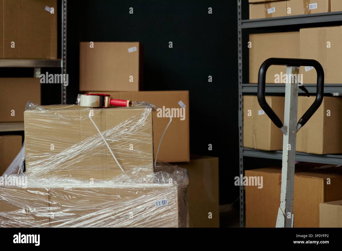 Nahaufnahme von Kartons, die auf Lagerregalen und Paletten stehen, für den Versand mit Klebebandspender und Palettenhubwagen verpackt. Ideal für E-Commerce-Logistik, Lagerung, Erfüllung Stockfoto