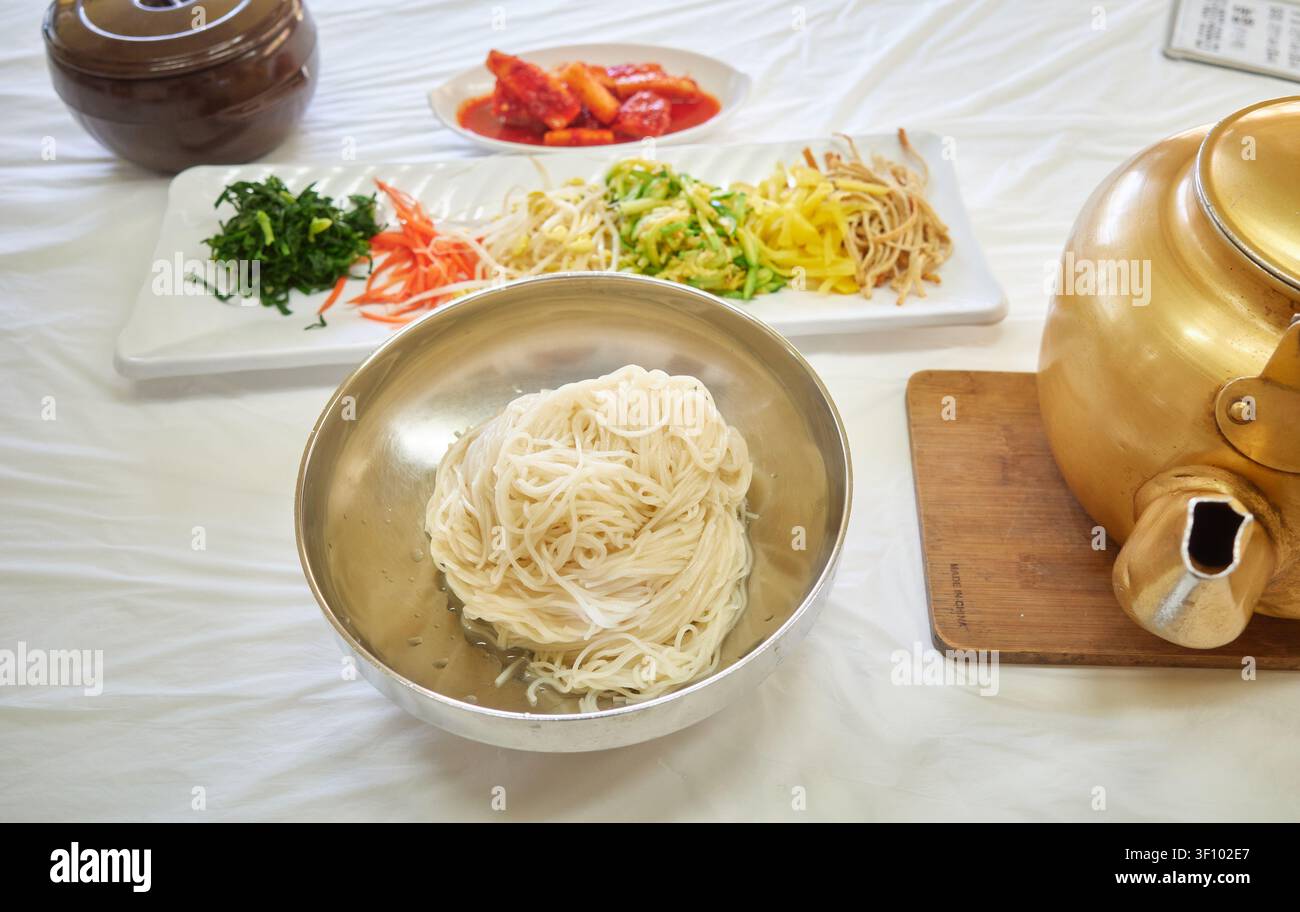 Traditionelle südkoreanische Bankettnudeln mit verschiedenen Gemüsebelägen und einem goldenen Messingkessel, der würzige Brühe einschenkt, die ein anpassbares DIY fängt Stockfoto