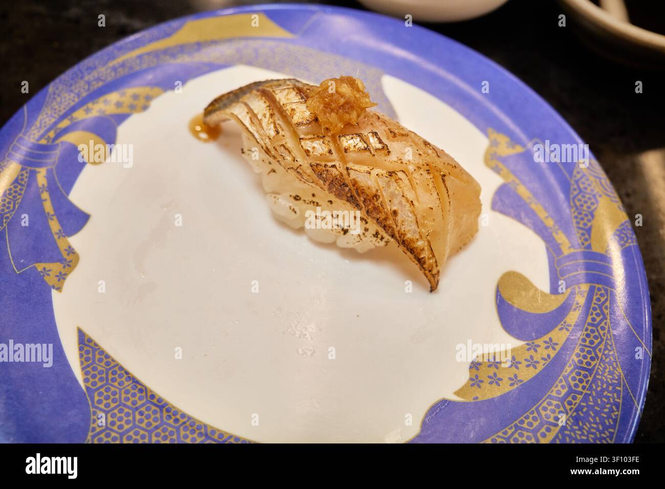 Verschiedene Premium-Nigiri-Sushi-Sorten, darunter frischer Weißfisch und gebratener Fisch mit Kreuzhatch-Schnitt, serviert auf bunten Tellern an einem modernen Transportband Stockfoto